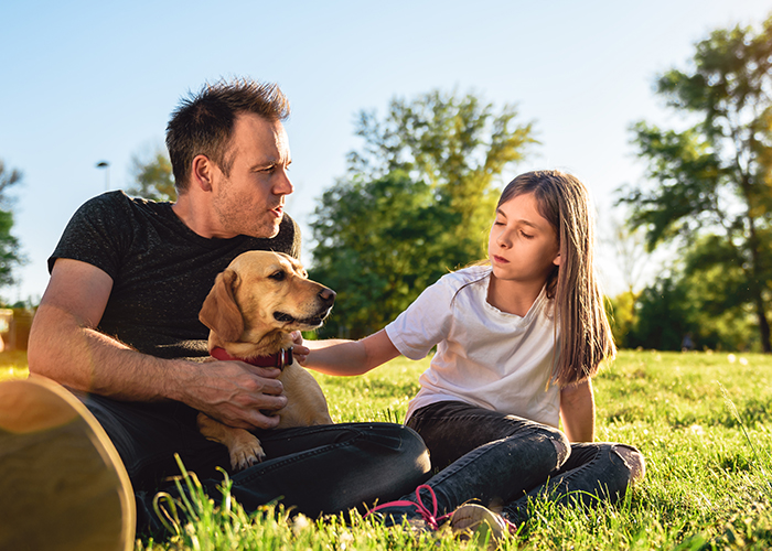 father and daughter talking, with dog in park