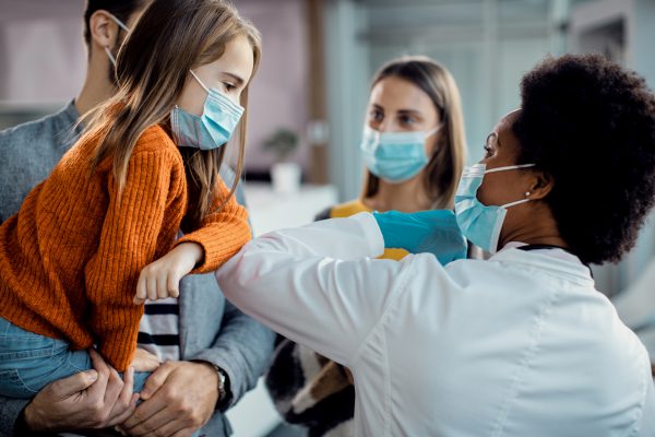 Small girl elbow bumping with a pediatrician while greeting at the clinic during coronavirus pandemic.