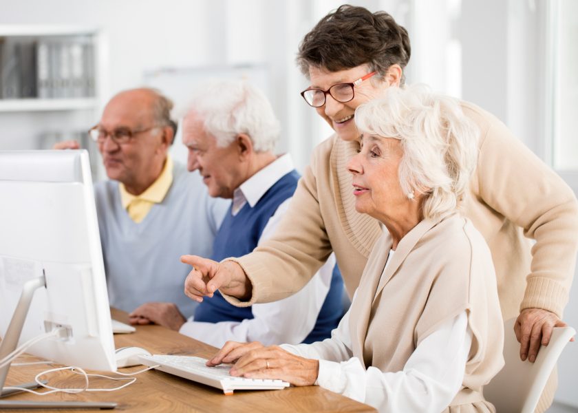 Woman showing another woman something on a computer, and two men looking at another computer screen.