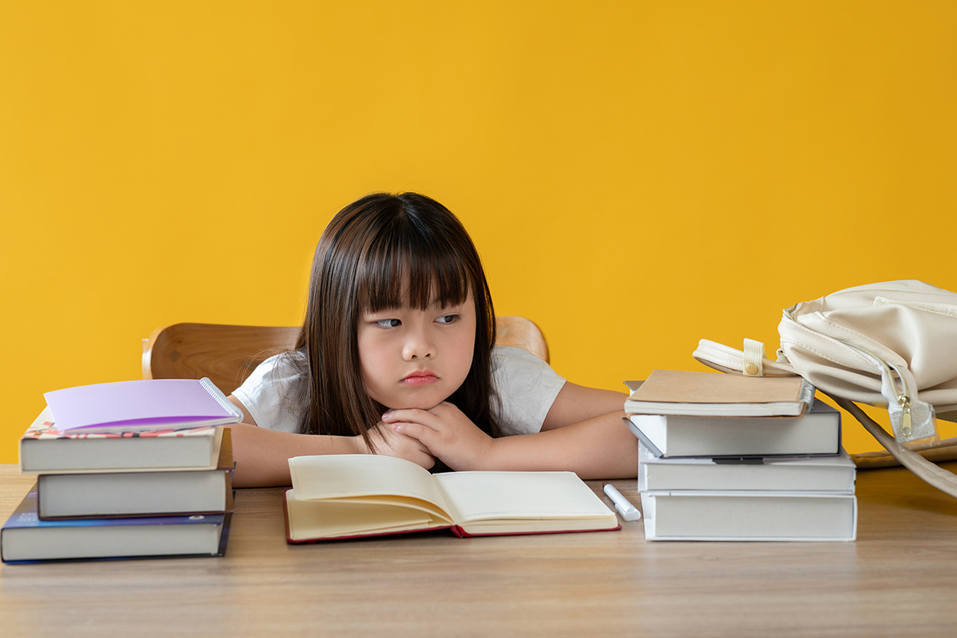 An adorable young girl sitting at her study table with a bored face, doesn't want to study or read