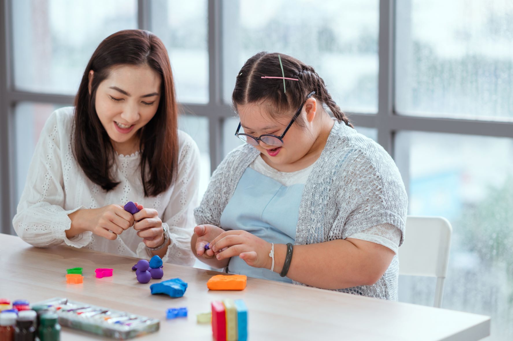 Two people crafting with colorful clay while sitting at a table, indoors on a rainy day