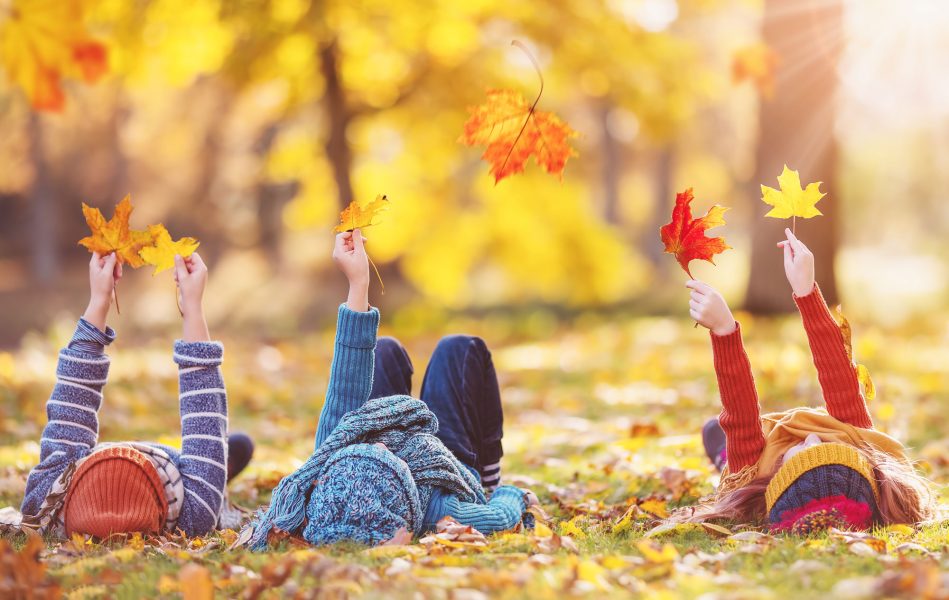 Children lying on the grass with maple leaves in their hands in autumnal park. Concept of the leisure in nature.
