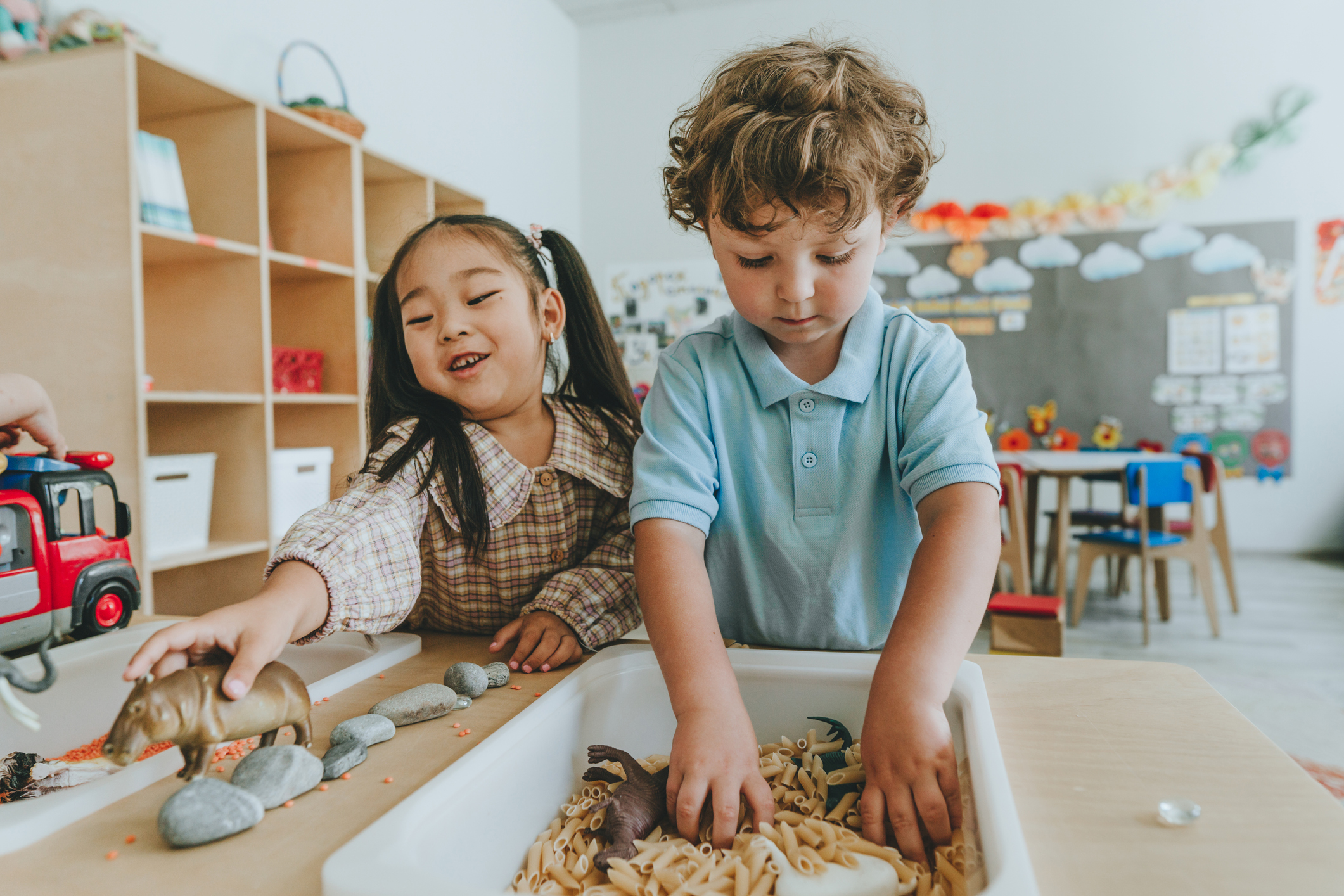 Children playing and developing tactility with toy animal figures in bulk cereals and pasta in kindergarten
