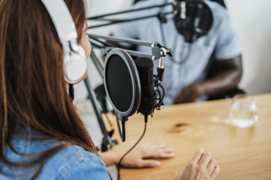 Young woman with headphones on speaking into a microphone across from a man