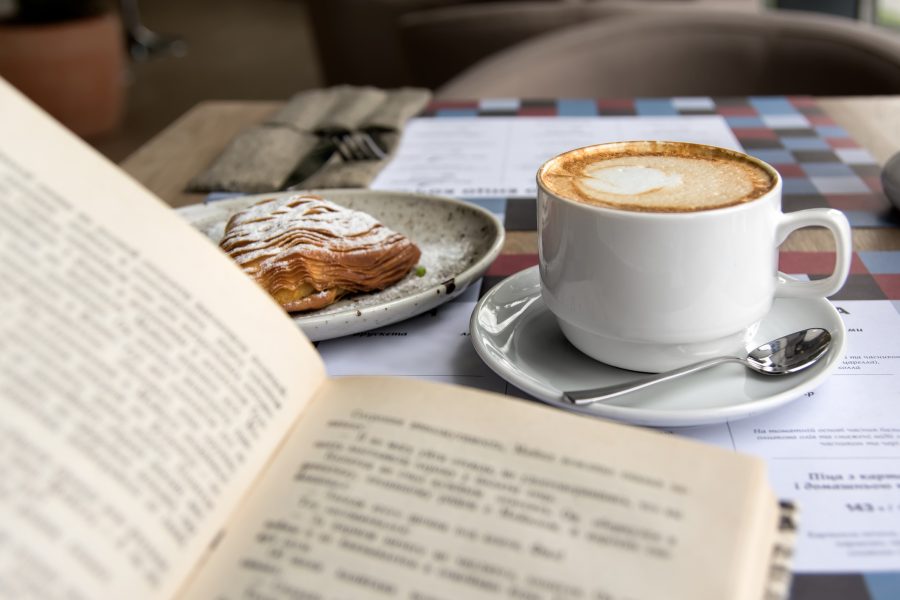 Reading a book with a hot beverage in a mug and a bakery treat on a plate