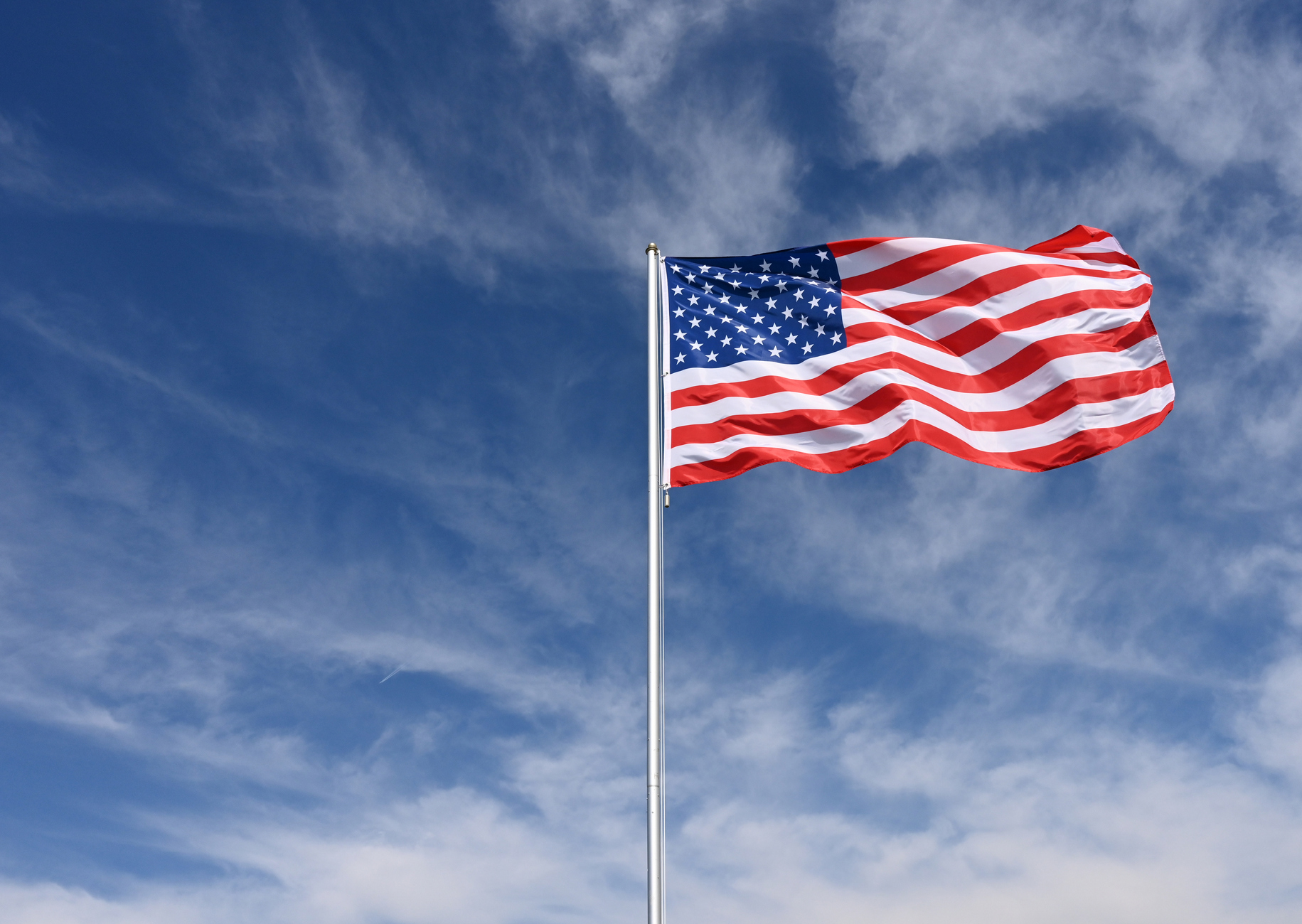US Flag flying against a blue sky with whispy white clouds